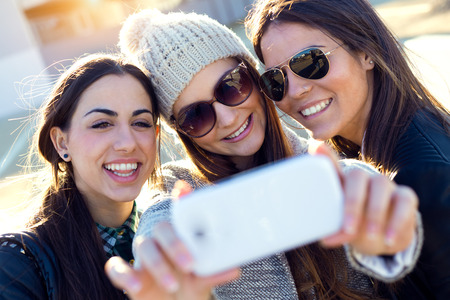 Portrait of three students girls using mobile phone in the campus.の写真素材