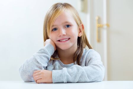 Portrait of beautiful blonde child sitting at a table in kitchen.