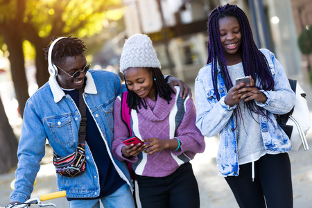 Portrait of group of three friends using mobile phone in the street.