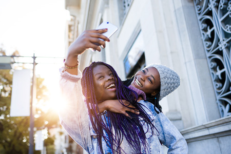 Portrait of two beautiful young woman using mobile phone in the street.の写真素材