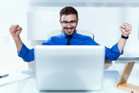 Portrait of handsome young businessman celebrating a victory while working with laptop in the office.の写真素材
