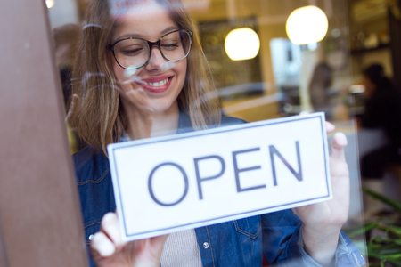 Portrait of beautiful young woman hanging the open sign on a glass door in the store.