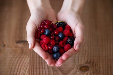 Close-up of some hands holding blueberries and raspberries over wooden background.