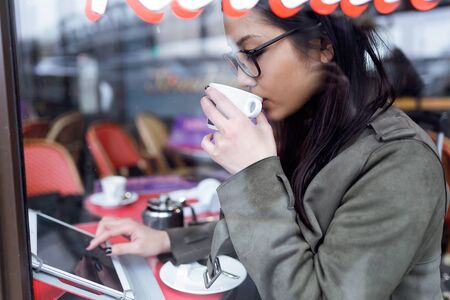 Shot of beautiful young asian woman using her digital tablet while drinking coffee in coffee shop.