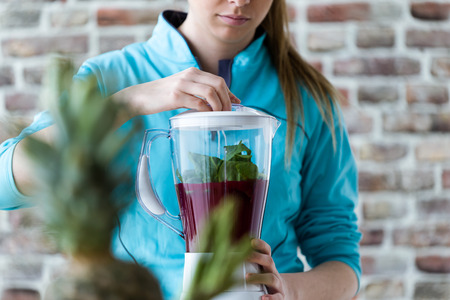 Close-up of beautiful young woman preparing detox juice in the blender at home.