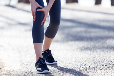 Close-up of fit and sporty young woman with leg pain in the forest. 