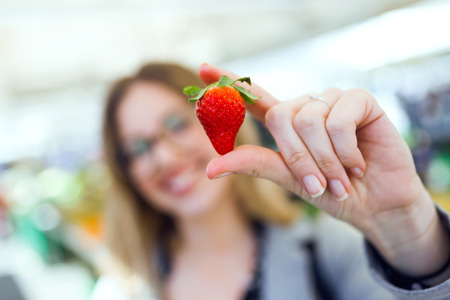 Shot of pretty young woman showing strawberry to camera in the street market.の写真素材