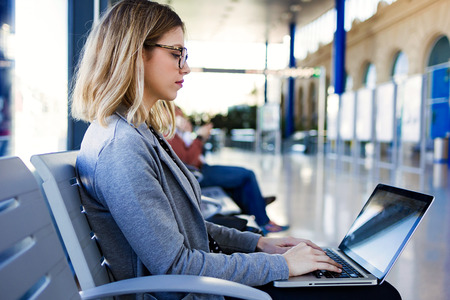 Shot of pretty young business woman using her laptop in the train station.の写真素材
