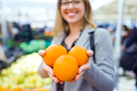 Shot of pretty young woman showing oranges to camera in the street market.の写真素材