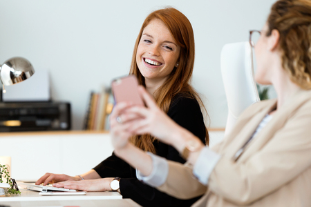 Shot of two pretty young business woman using her mobile phone in the office.の写真素材