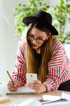 Shot of pretty young architect woman working on a blueprints while talking on the phone in the office.の写真素材