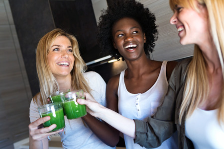 Shot of pretty young women toasting with detox green juice and smiling at home.の写真素材