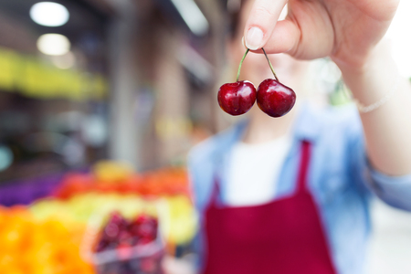 Shot of pretty young saleswoman showing cherries to camera in health grocery shop.の写真素材