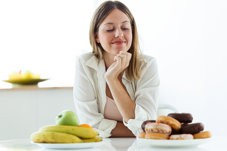 Shot of pretty young woman choosing between fruit and sweet at home.の写真素材