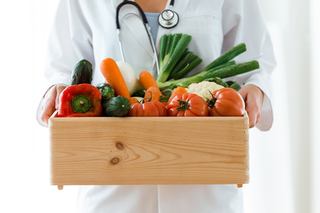Close-up of nutritionist holding wooden box with fresh vegetables over white background.の写真素材