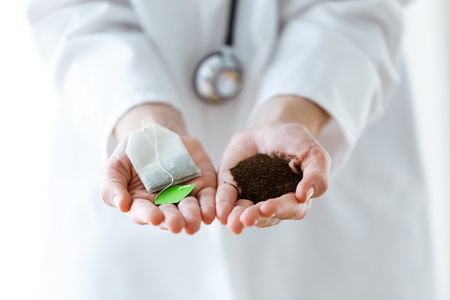 Close-up of nutritionist holding tea bag in one hand and dry tea in the other hand over white background.の写真素材