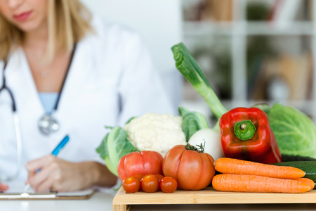 Shot of beautiful young nutritionist working at desk and writing medical records over fresh fruit in the consultation.の写真素材