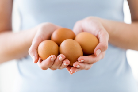 Close-up of young woman holding brown chicken eggs over white background.の写真素材