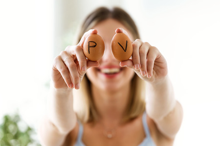 Shot of beautiful young woman covering her eyes with brown chiken eggs at home.の写真素材