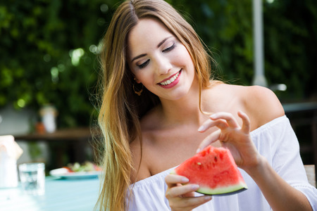 Portrait of beautiful young woman eating watermelon in the home garden.の写真素材