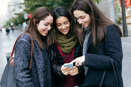 Outdoor portrait of three young beautiful women using mobile phone.の写真素材