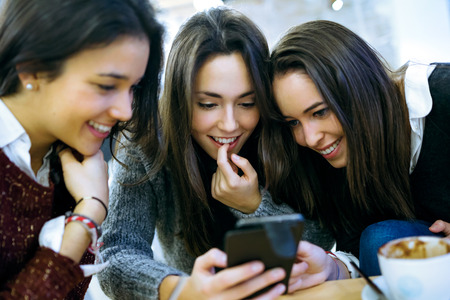 Portrait of three young beautiful women using mobile phone at cafe shop.の写真素材