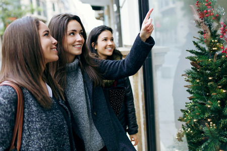 Outdoor portrait of three young beautiful women looking at the shop window.の写真素材