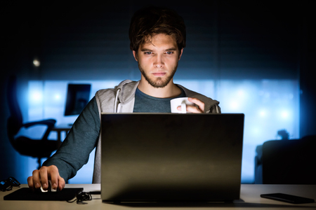 Portrait of handsome young man working with laptop in his office at night.の写真素材