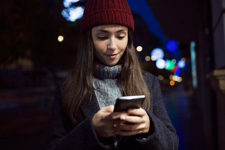Outdoor portrait of beautiful young woman using her mobile phone at night.の写真素材