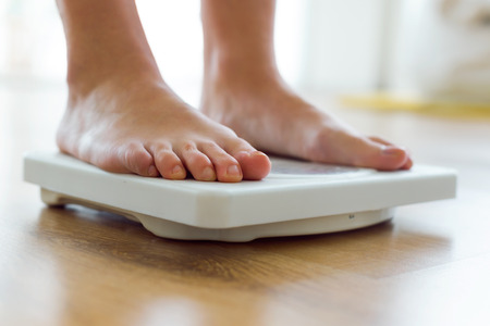 Portrait of young healthy girl on home scales.