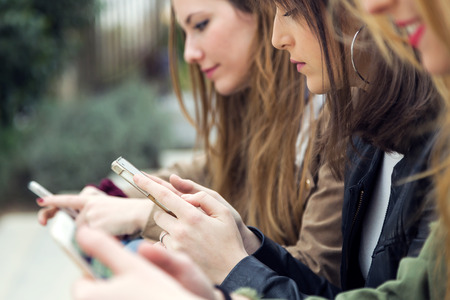 Portrait of three young women using a mobile phone in the street.の写真素材