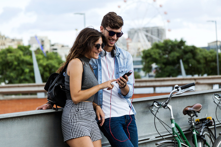Portrait of happy young couple using mobile phone in the street.の写真素材