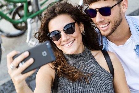 Portrait of happy young couple using mobile phone in the street.の写真素材