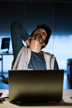 Portrait of handsome young man working with laptop in his office at night.の写真素材