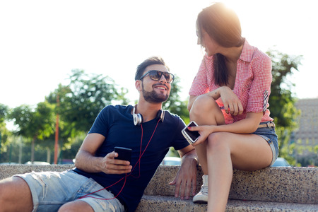 Portrait of two friends using mobile phone and listening to music in the street.の写真素材