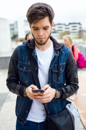Portrait of handsome student using mobile phone in the street.の写真素材