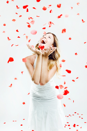 Portrait of beautiful young woman under a rain of rose petals. Isolated on white.の写真素材