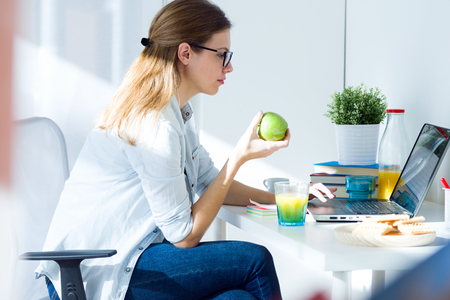 Portrait of pretty young woman eating an apple and working at home.の写真素材
