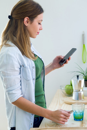 Portrait of beautiful young woman using her mobile phone and enjoying breakfast.の写真素材