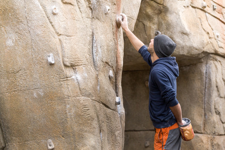Portrait of handsome young man starting to climb on natural rocky wall.