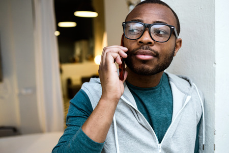 Portrait of handsome young black man using his mobile phone at home.の写真素材