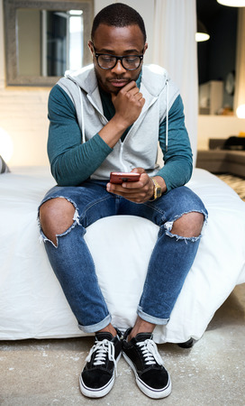 Portrait of handsome young black man using his mobile phone at home.の写真素材