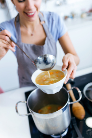 Portrait of young woman serving vegetable soup in the kitchen.の写真素材