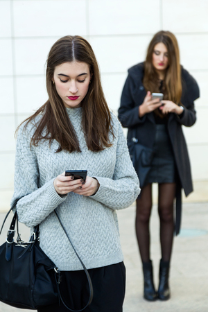 Portrait of two young businesswoman using mobile phone in the street.の写真素材