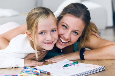Portrait of young mother and daughter drawing on the notebook at home.