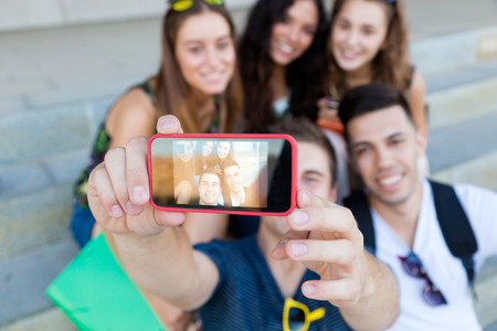 Outdoor portrait of group of friends taking photos with a smartphone in the street.の写真素材
