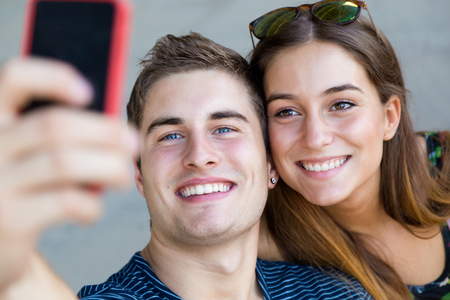 Portrait of young students taking photos with a smartphone in the street.の写真素材