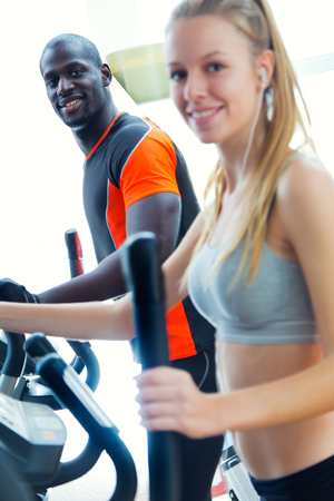 Portrait of young people with elliptic machine in the gym.