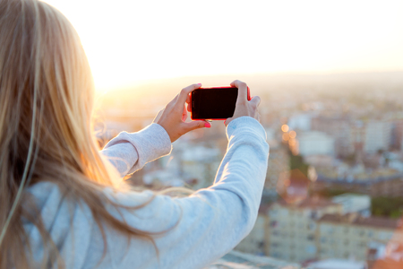Outdoor portrait of beautiful blonde girl taking pictures of the city.の写真素材