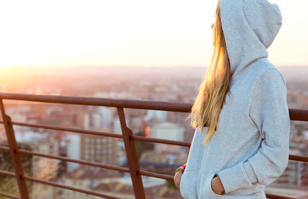 Outdoor portrait of beautiful blonde stands on the edge of the roof.の写真素材